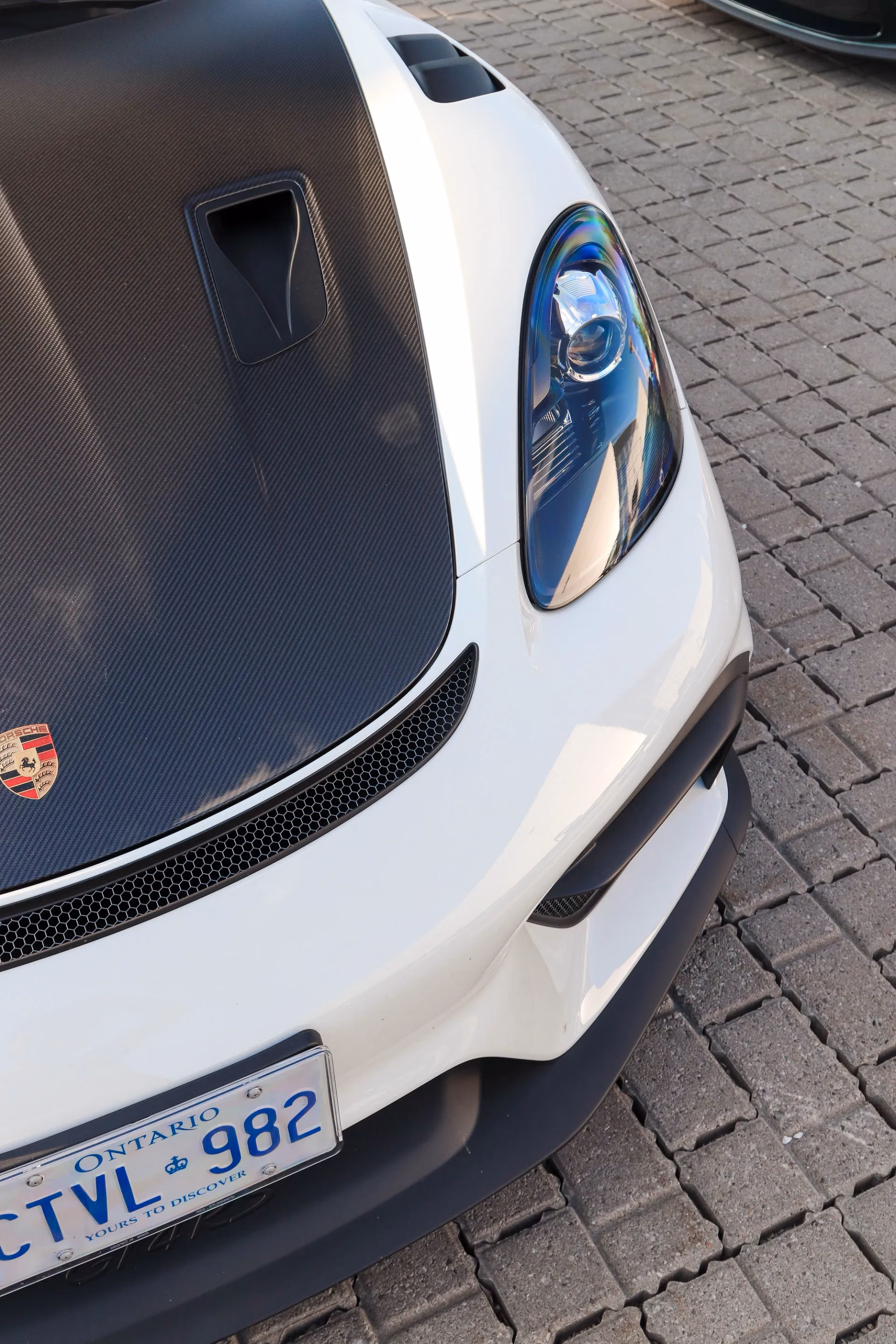 Close-up of a white Porsche Cayman's carbon hood, crest and Ontario licence plate