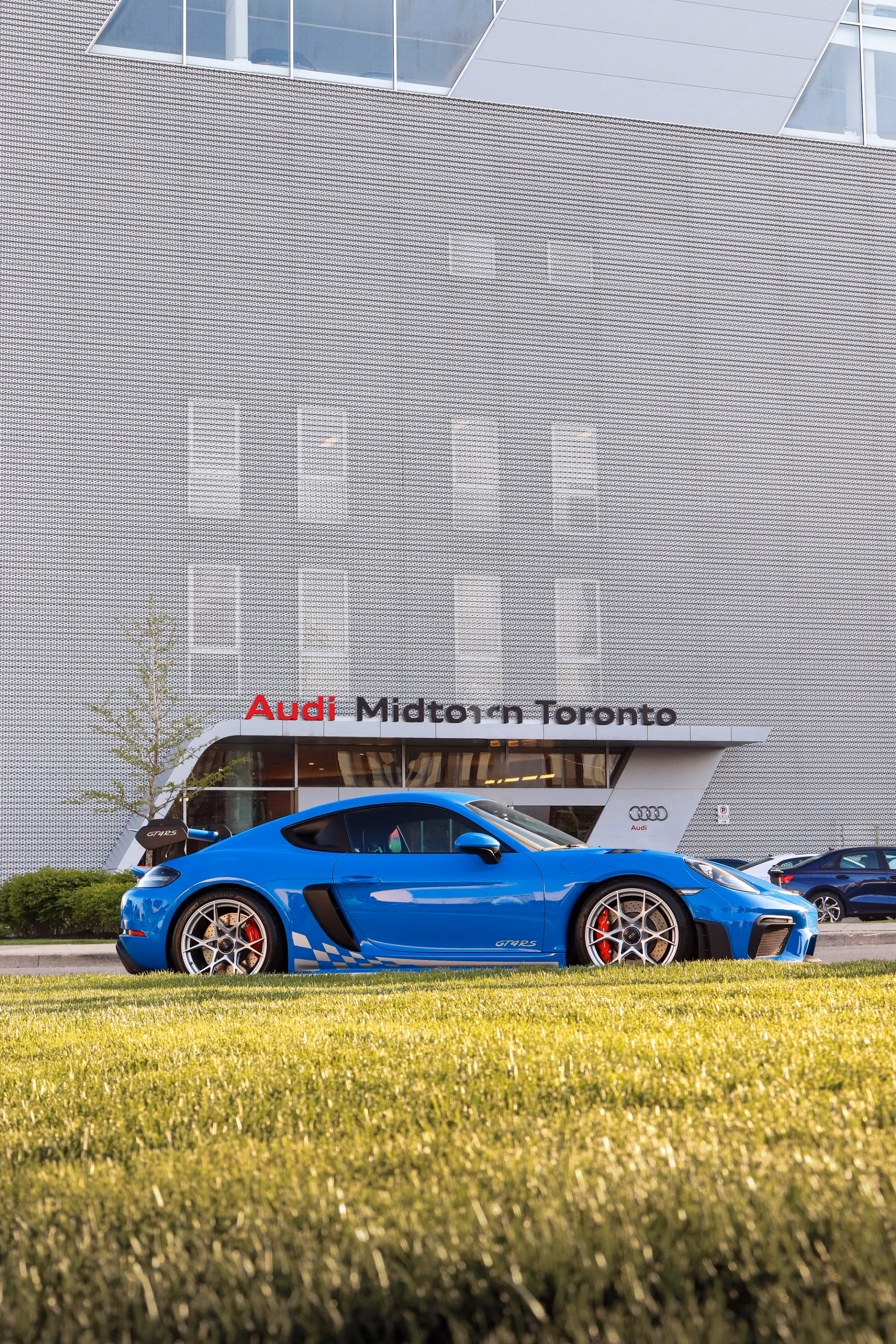 A blue Porsche Cayman GT4 RS parked in profile outside the Audi Midtown Toronto building
