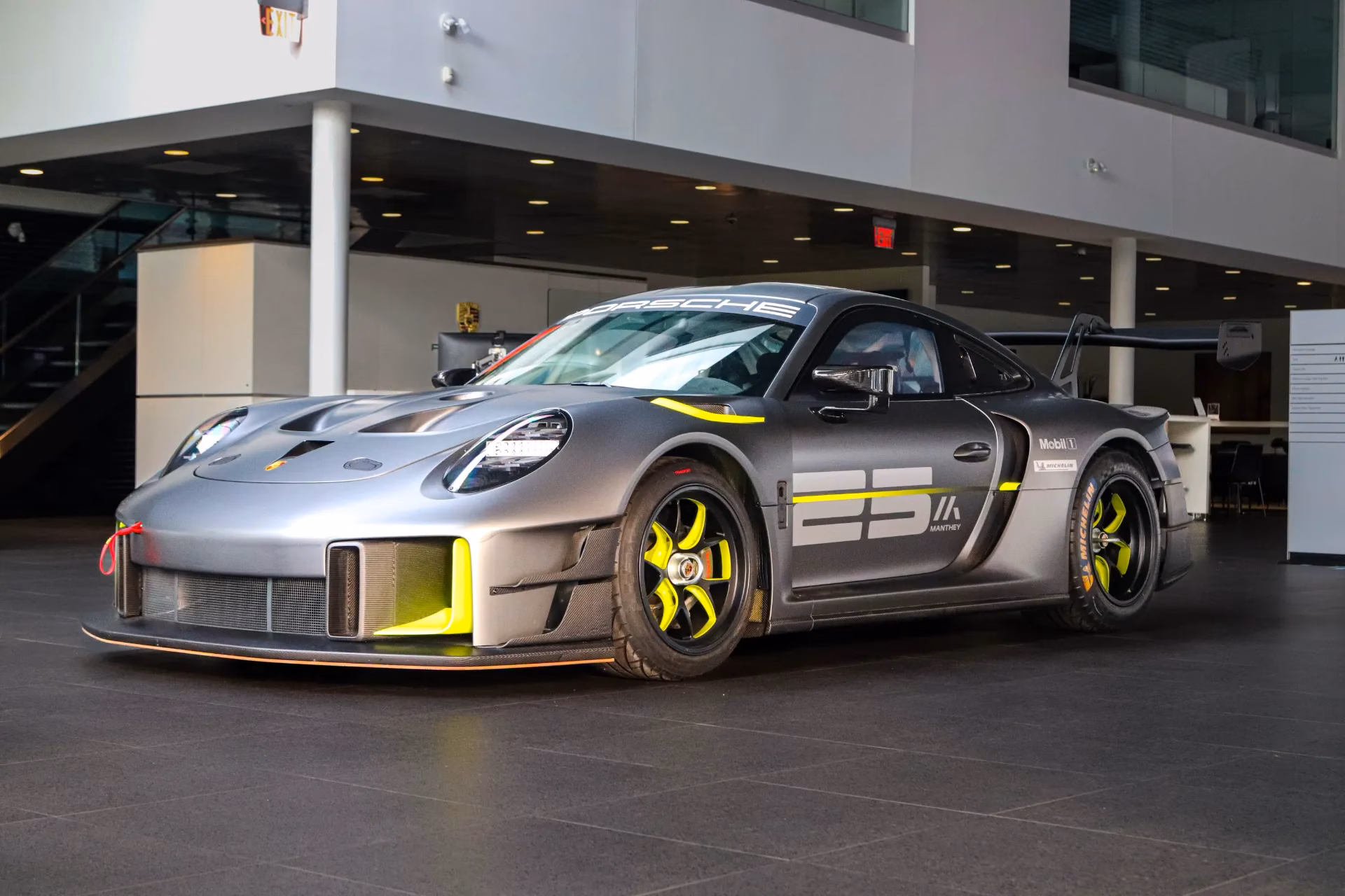 A silver Porsche 911 race car with yellow accents and a roll cage on display in a showroom