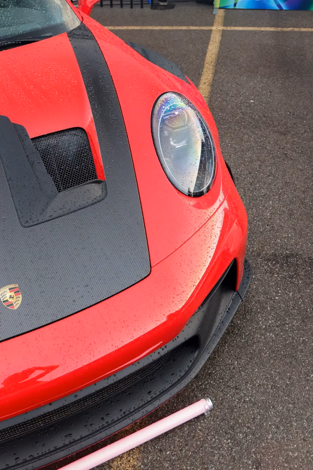 Close-up of a red Porsche 911's carbon hood, headlight and crest in the rain