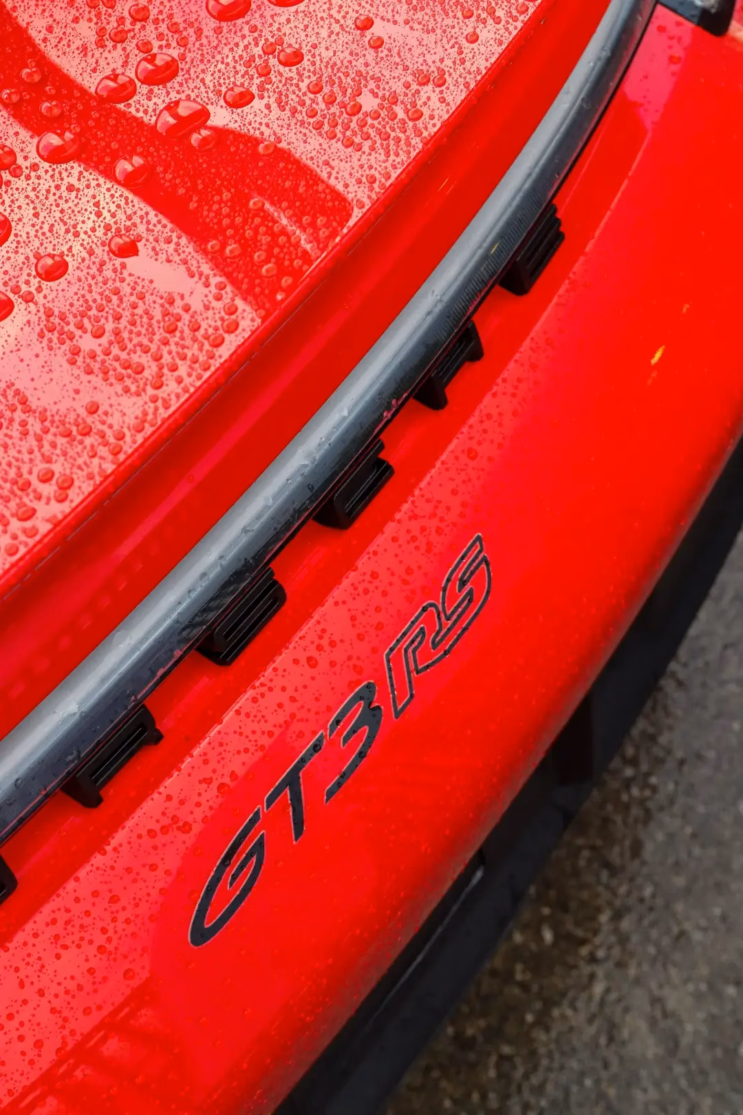 Close-up of the GT3 RS badge on the rear of a red Porsche, beaded with rain