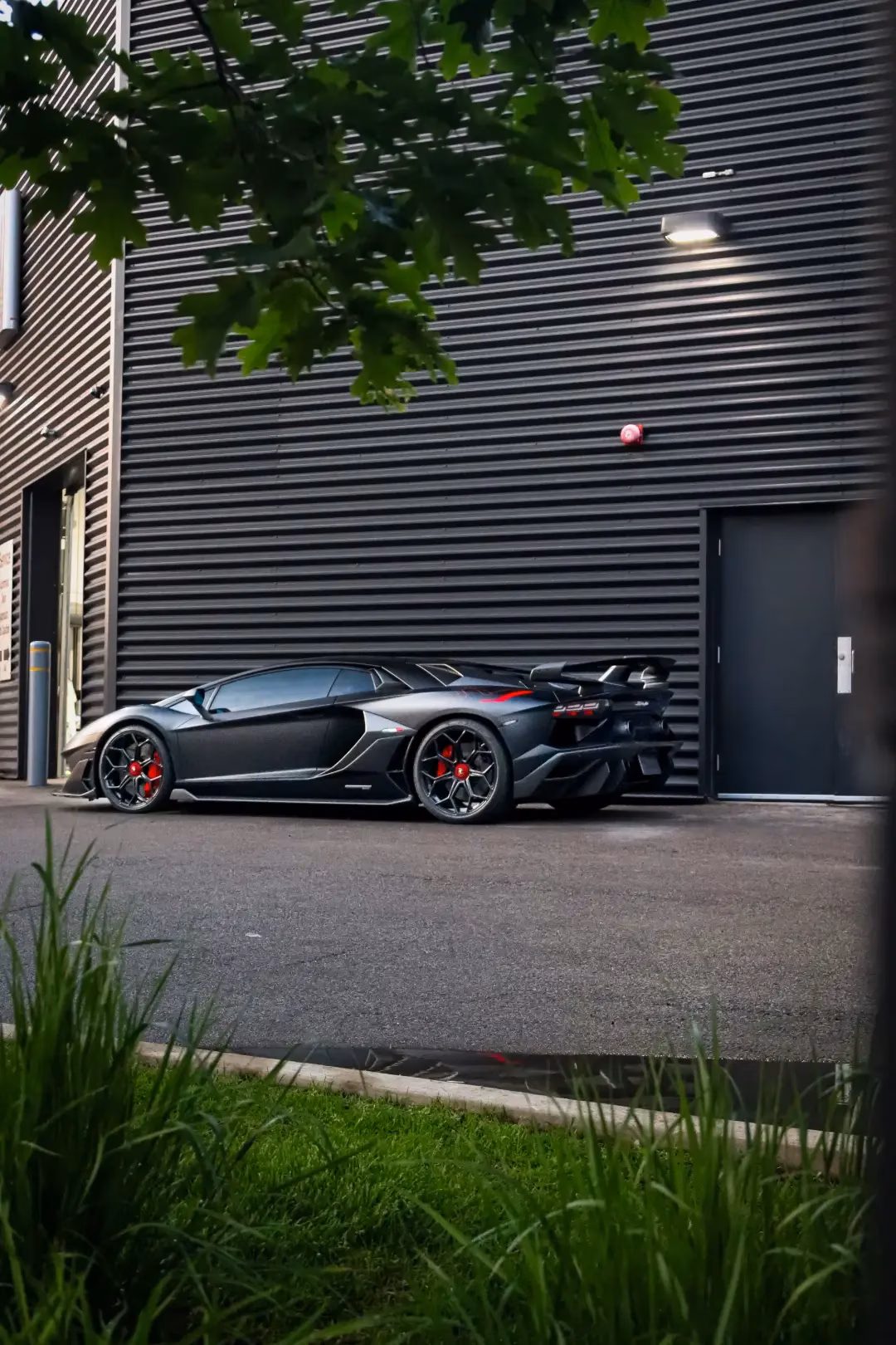 A grey Lamborghini Aventador parked beside a slatted building