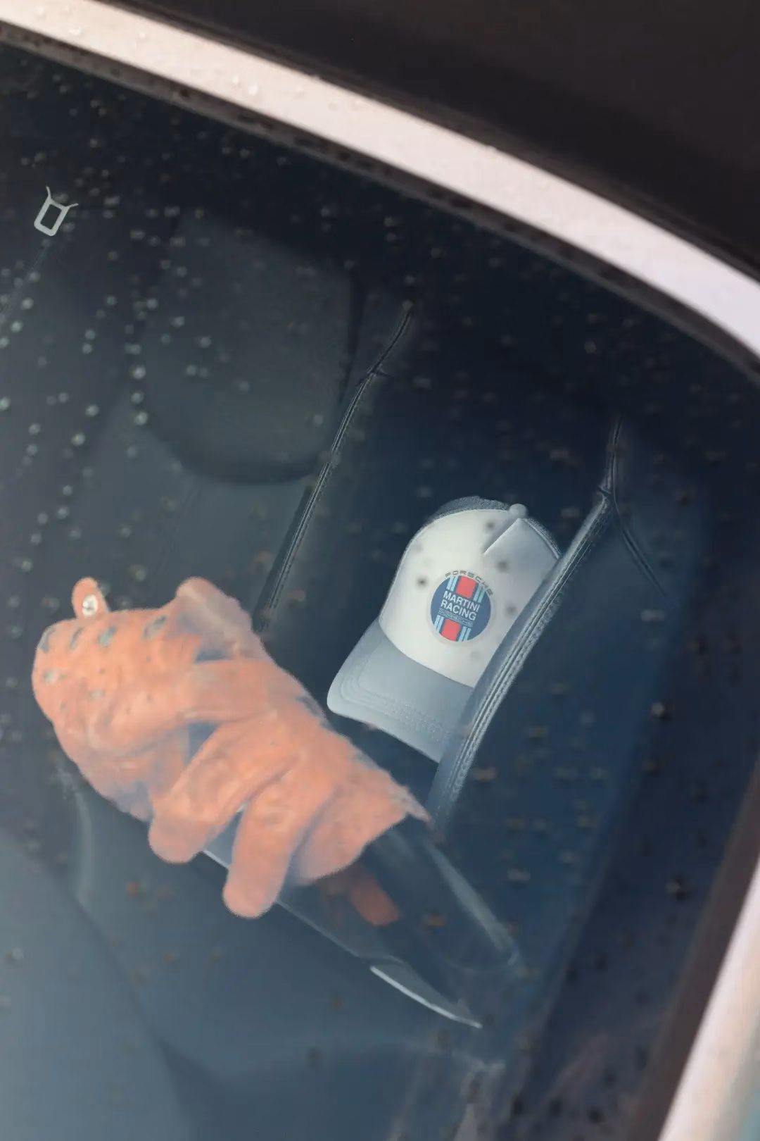 An orange driving glove and a cap resting on a dashboard, seen through the windscreen