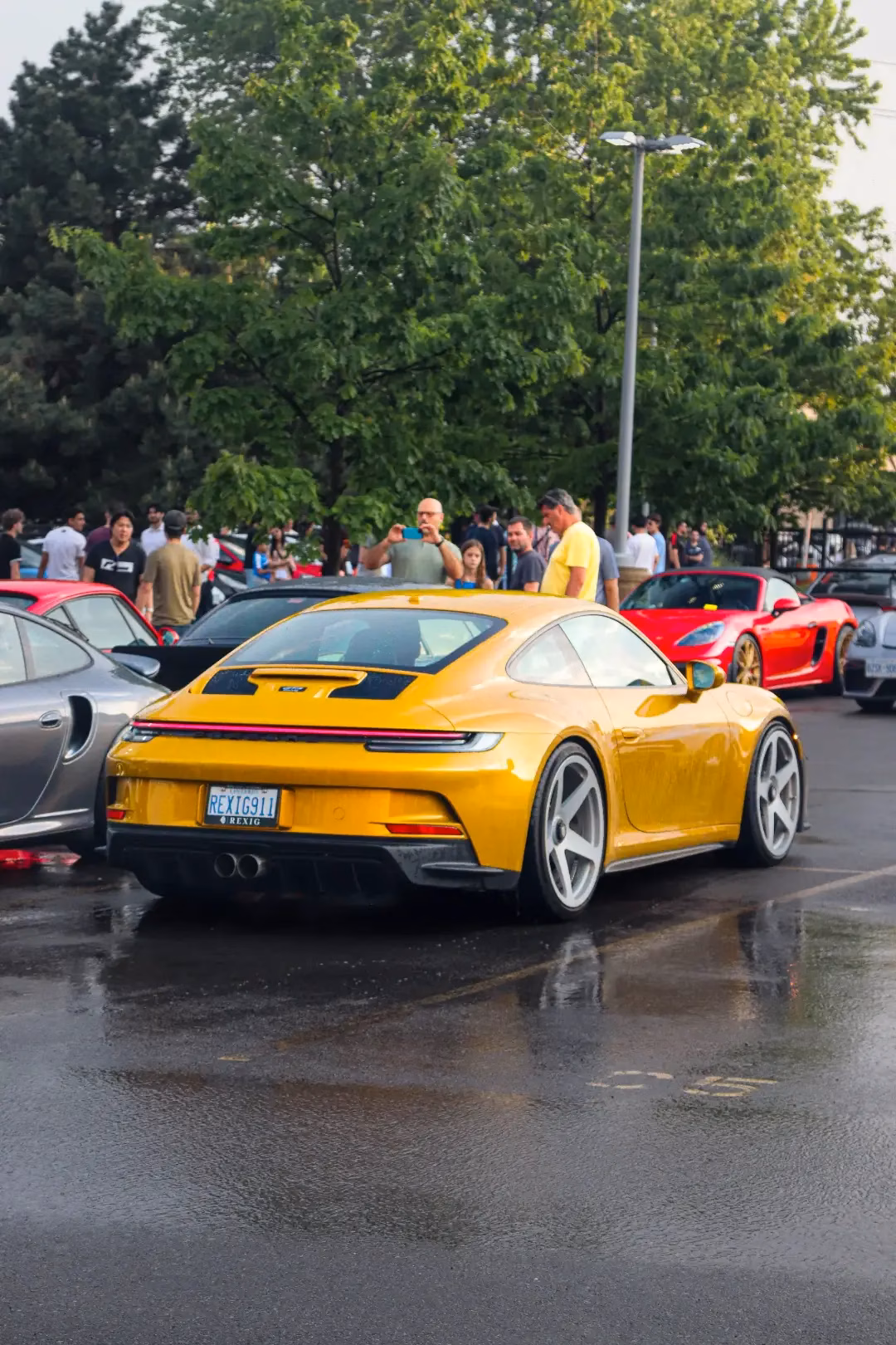 A yellow Porsche 911 parked at a wet evening meet, members gathered behind