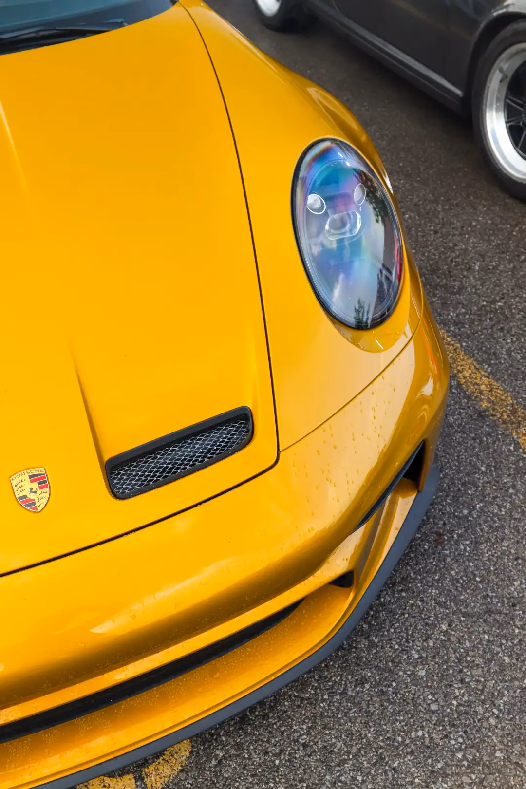 Close-up of a yellow Porsche 911's headlight, hood vent and crest