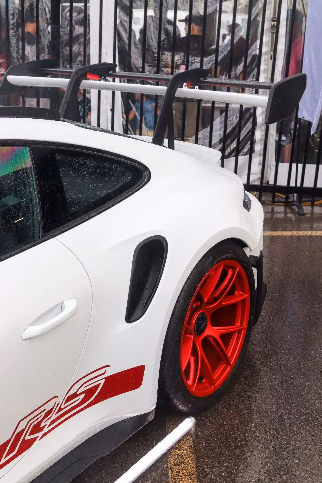 Rear quarter of a white Porsche 911 GT3 RS with red wheels and a swan-neck rear wing in the rain