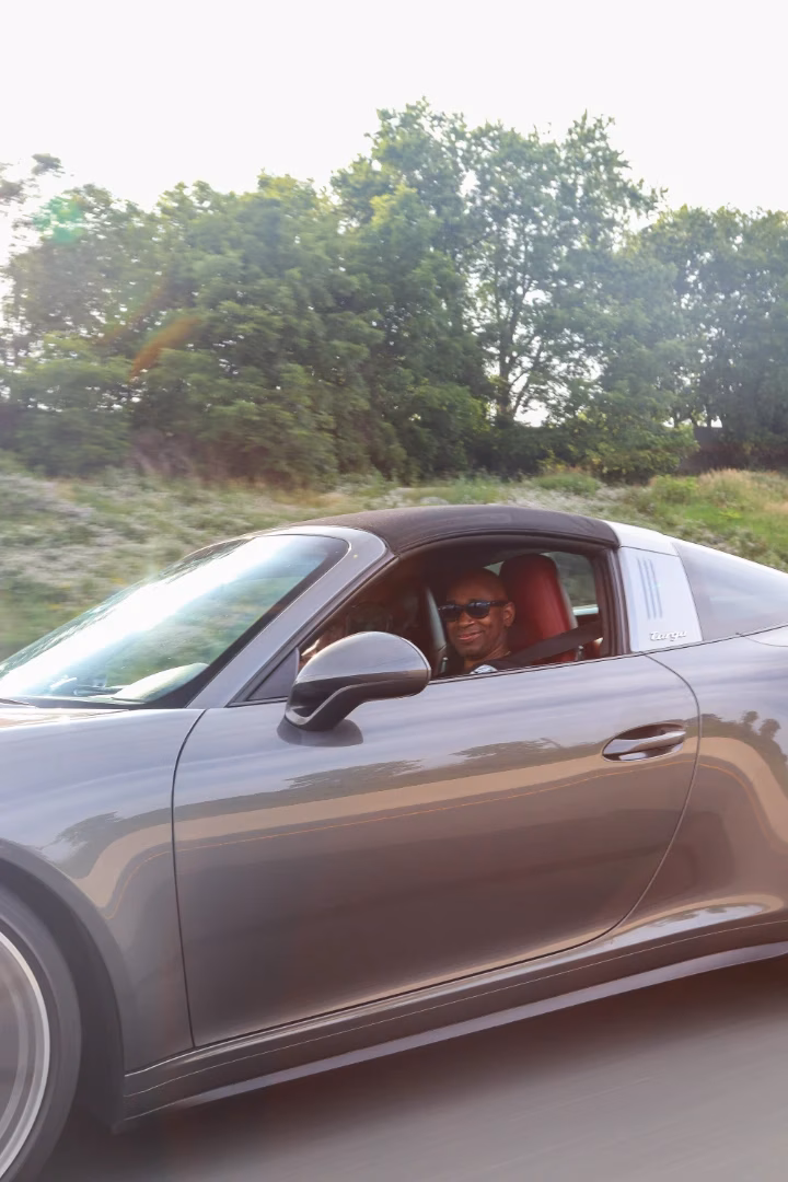 A grey Porsche 911 Targa on the move, the driver visible through the side window