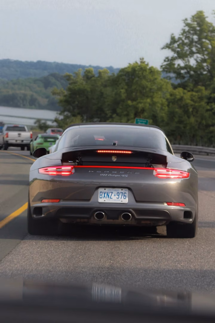 Rear of a grey Porsche 911 Targa on the highway, a lake in the distance