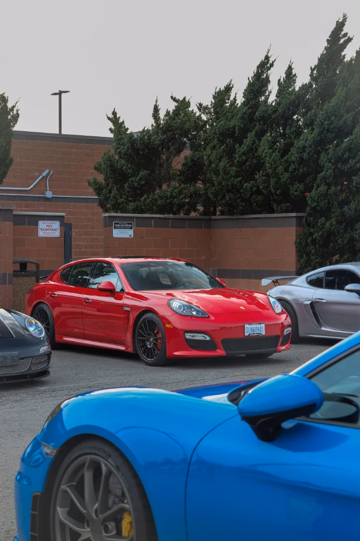 A red Porsche Panamera parked in a lot, a blue Porsche in the foreground