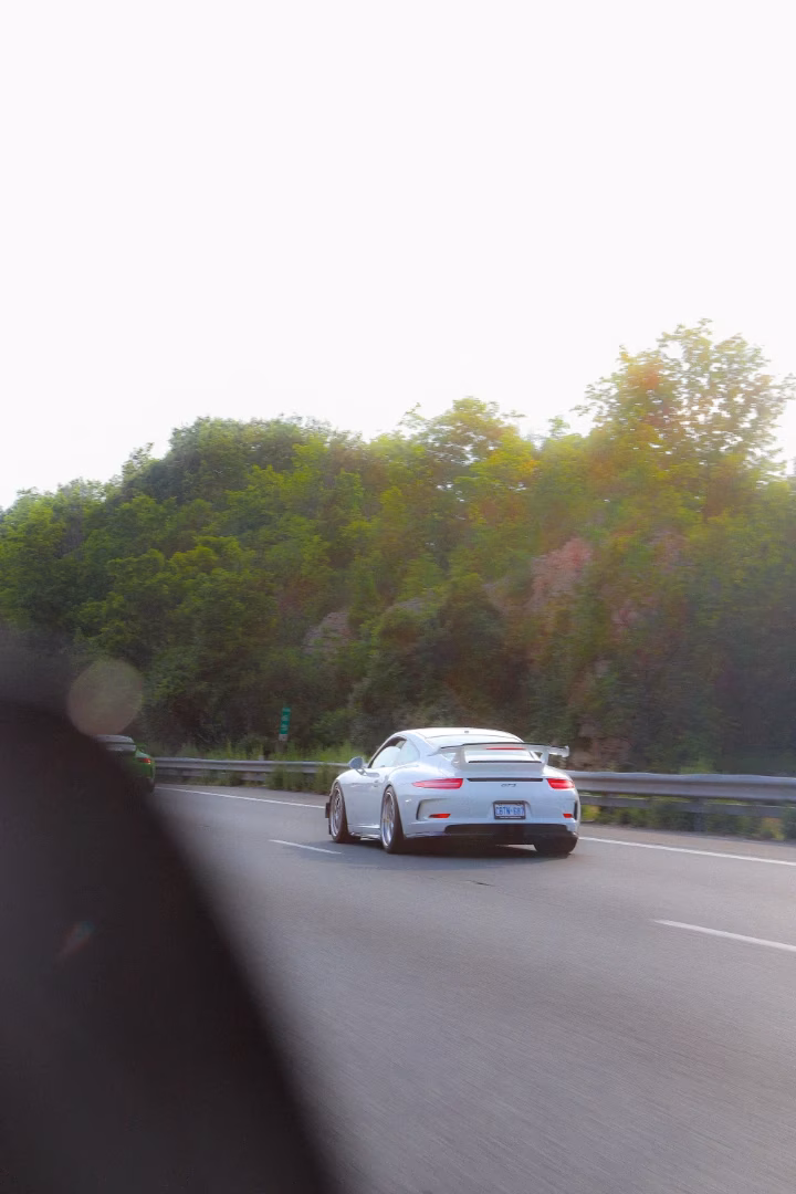 A white Porsche 911 GT3 on the highway beside a wooded hillside