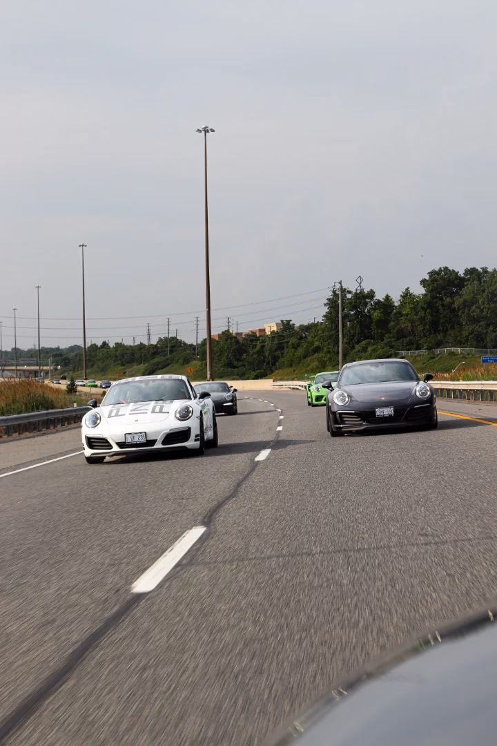A white and a grey Porsche 911 on the highway, a green Porsche following