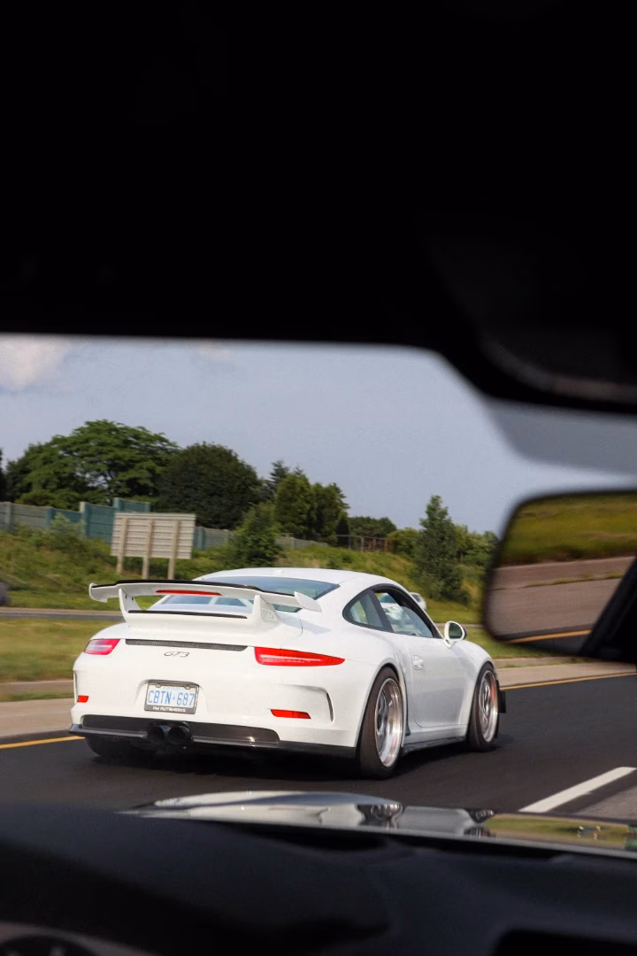 A white Porsche 911 GT3 on the highway, seen through the rear window of another car