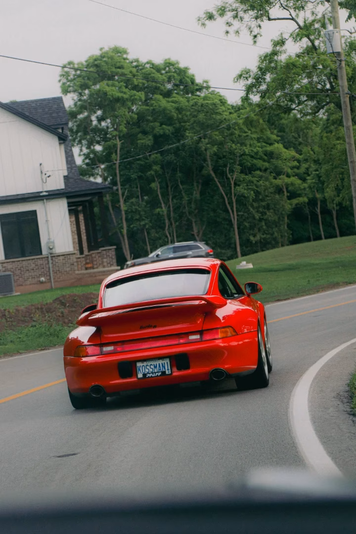 A red classic Porsche 911 on a road past a house