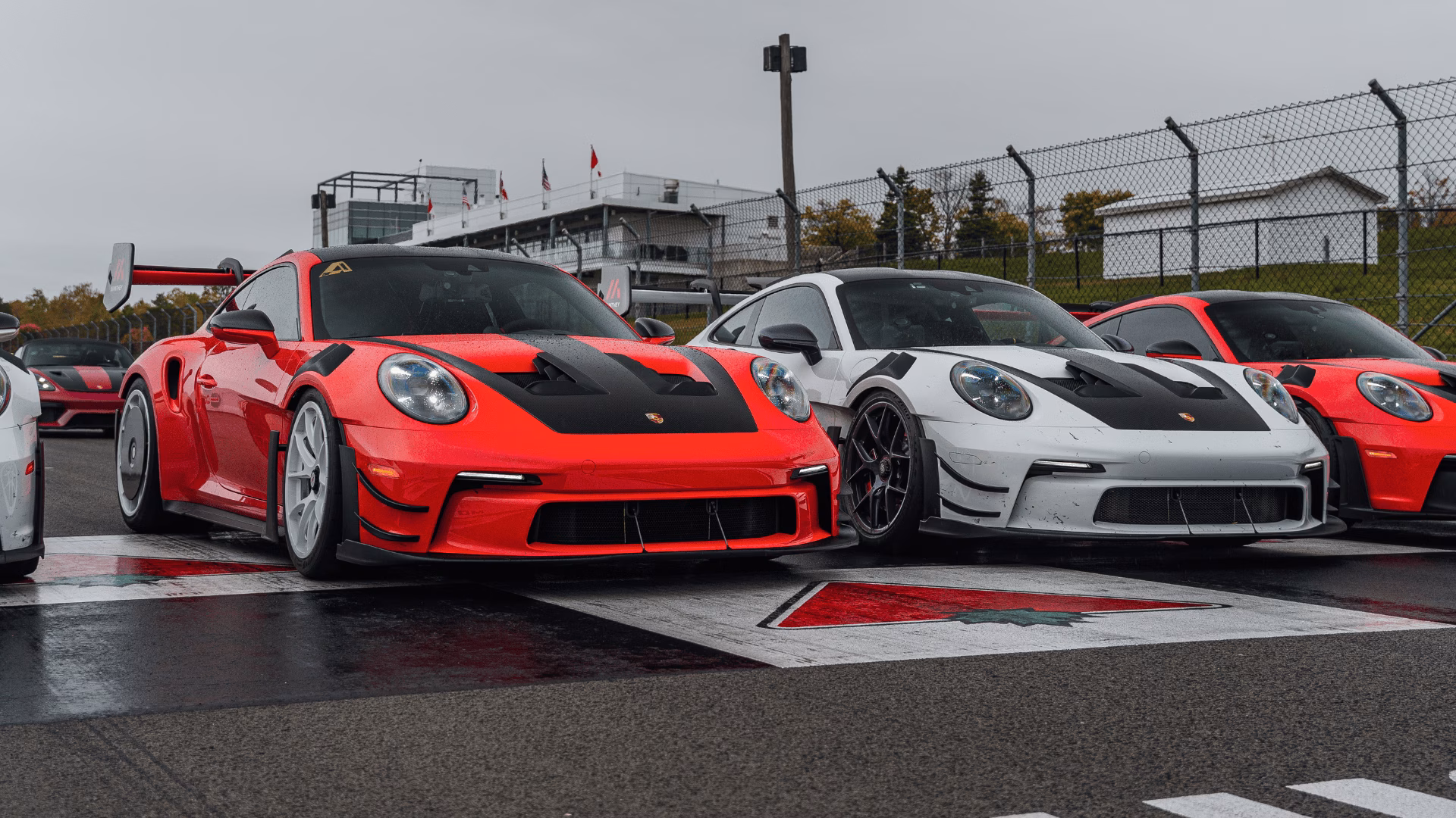 A red and a white Porsche 911, both with large rear wings, parked side by side on a track start line