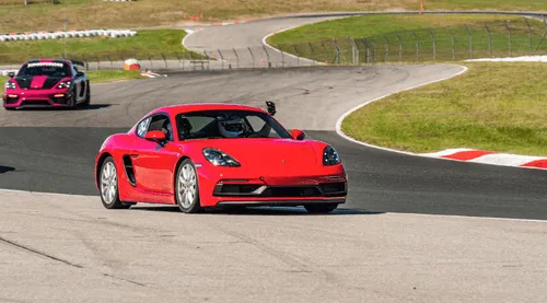 A red Porsche 718 Cayman on track, a pink race car following