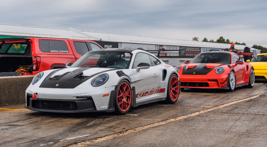 A white Porsche 911 GT3 RS with red wheels beside a red GT3 RS in the pit lane