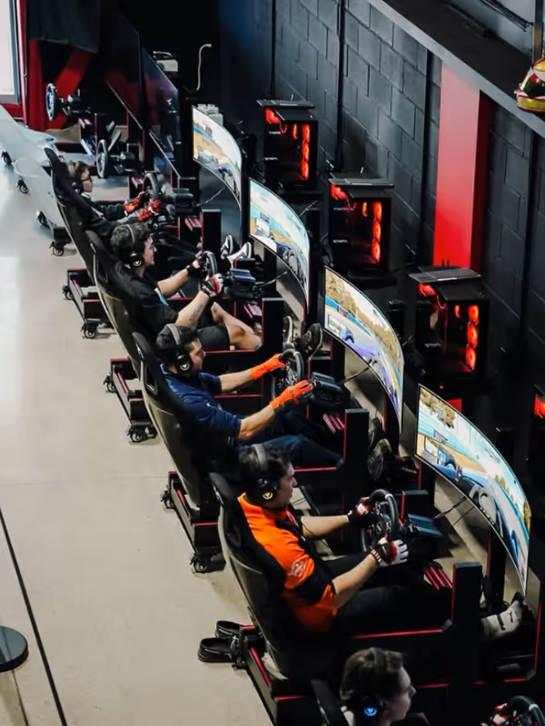 A row of drivers racing in sim rigs, each at their own screen